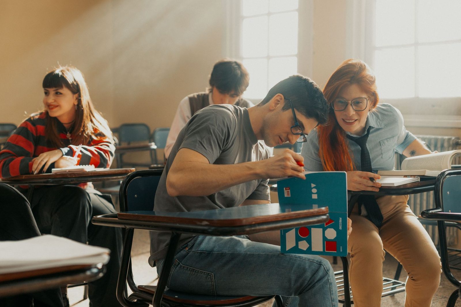 Students writing at desks in a sunlit classroom during a group class.